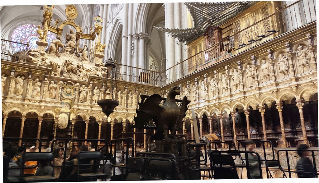 На изображении представлен интерьер Толедского собора (Catedral Primada Santa María de Toledo) в Испании.Хор (Coro): На переднем плане видна центральная часть хора собора.Деревянная резьба: Скамьи хора выполнены с детальной готической и ренессансной резьбой